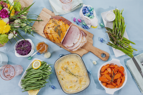 Easter Table Setting. Pretty light blue table green beans, scalloped potatoes, bowl of carrots. cloth with Ham on a cutting board, plate of 