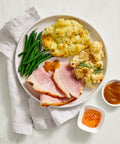 Plated meal with Denninger's ham, green beans, mashed potatoes, and cauliflower on a marble surface.
