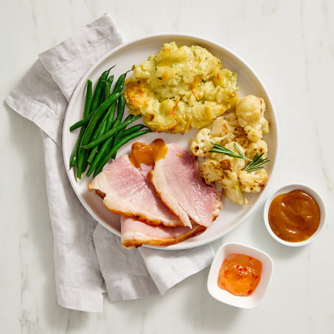 Plated meal with Denninger's ham, green beans, mashed potatoes, and cauliflower on a marble surface.