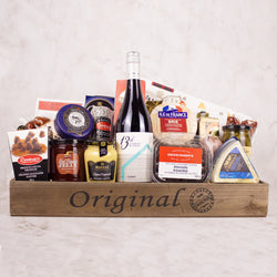 A wooden crate with gourmet assortment of cheese, crackers, cured and smoked meats, olives, pickles and sweets with a bottle of  13th Street Winery's Gamey 2021.