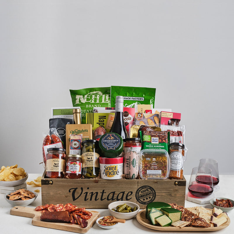 A wooden crate with gourmet assortment of cheese, crackers, cured and smoked meats, olives, pickles and sweets with a bottle of 13th Street Wine.