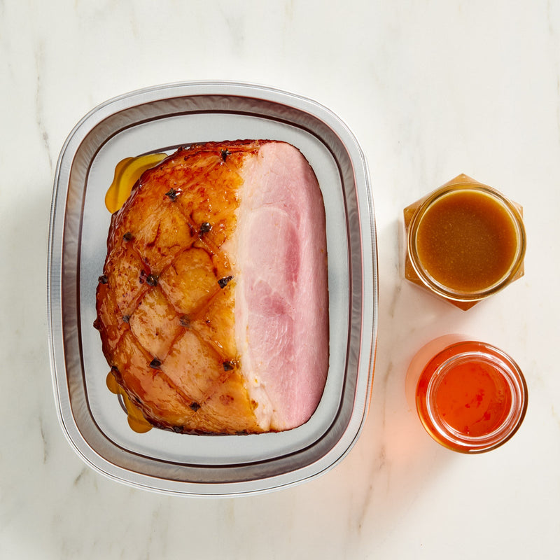 Denninger's Virginia ham in a silver foil container with two small jars of condiments on a marble surface