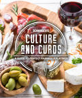 A styled food spread on wooden boards with cured meats, cheeses, olives, bread, and a glass of red wine, overlaid with the text 'Denninger's Culture and Curds: A Guide to Perfect Pairings & Plating'.