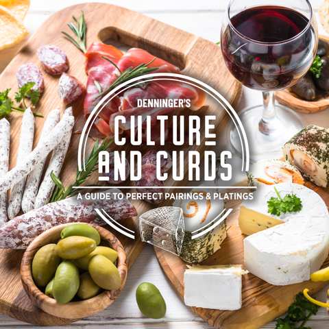 A styled food spread on wooden boards with cured meats, cheeses, olives, bread, and a glass of red wine, overlaid with the text 'Denninger's Culture and Curds: A Guide to Perfect Pairings & Plating'.