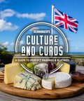 A styled cheese board outdoors on a wooden table under a Union Jack flag, with a large overlaid title reading 'Denninger's Culture and Curds: A Guide to Perfect Pairings & Platings.' The scene includes multiple cheeses, grapes, crackers, and a small bowl of spread against a blue sky and landscape background.