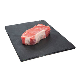 250 gram raw AAA Canadian Beef: Striploin Steak displayed on a black slate board. Aged for 21 days.