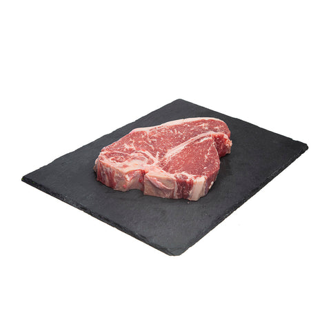 650 gram piece of raw AAA Canadian Beef:  T-Bone Steak displayed on a  black slate board.